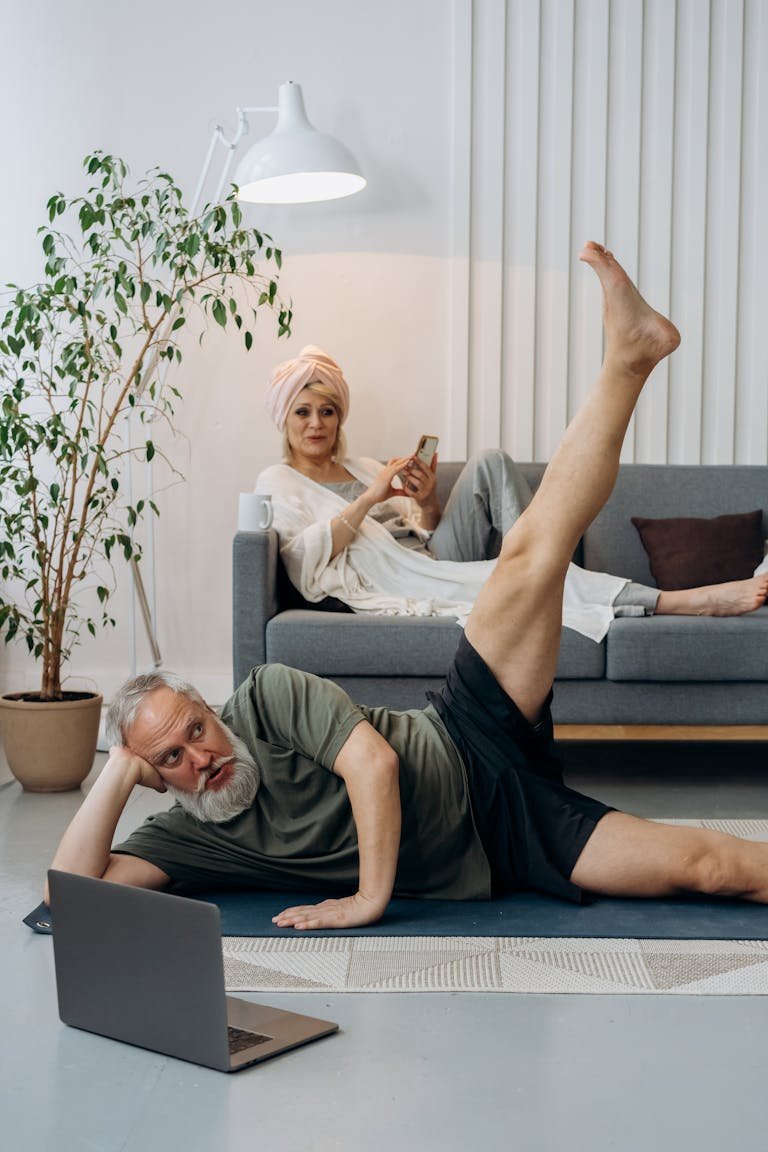 Elderly couple balancing fitness and relaxation at home, with yoga and online exploration.