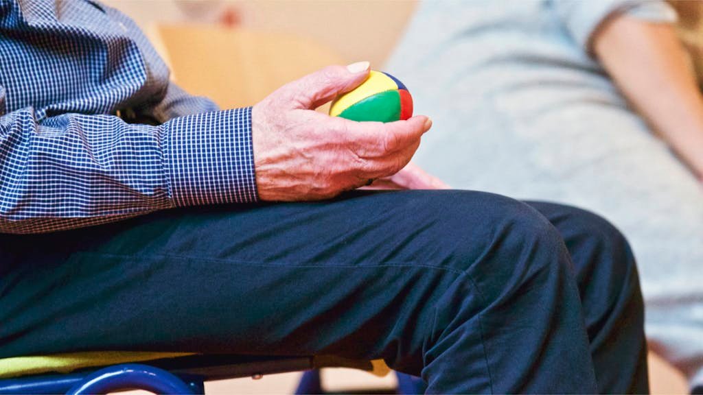 Elderly man holding a colorful therapy ball indoors, promoting relaxation and health.