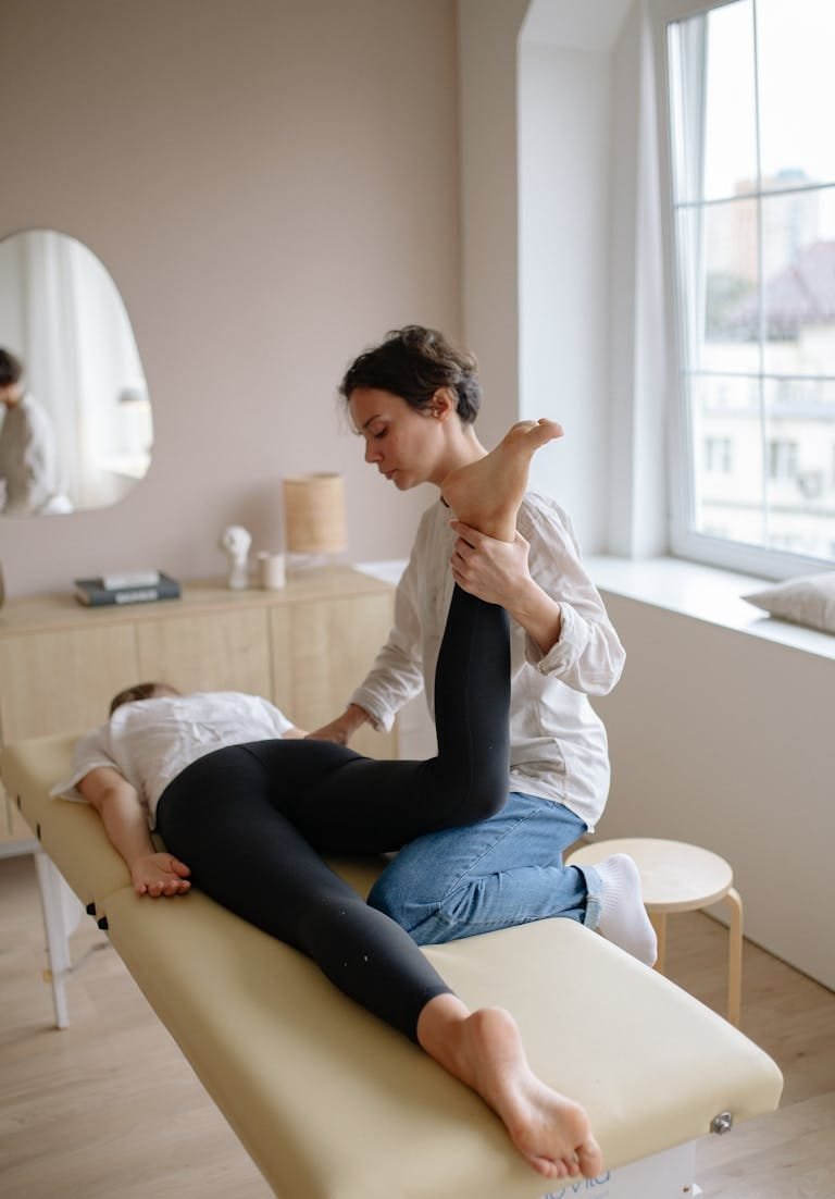 Physiotherapist aiding a woman with leg exercises on a massage table for relaxation and therapy.