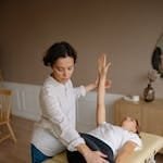 Physiotherapist aids woman with therapeutic exercises indoors.