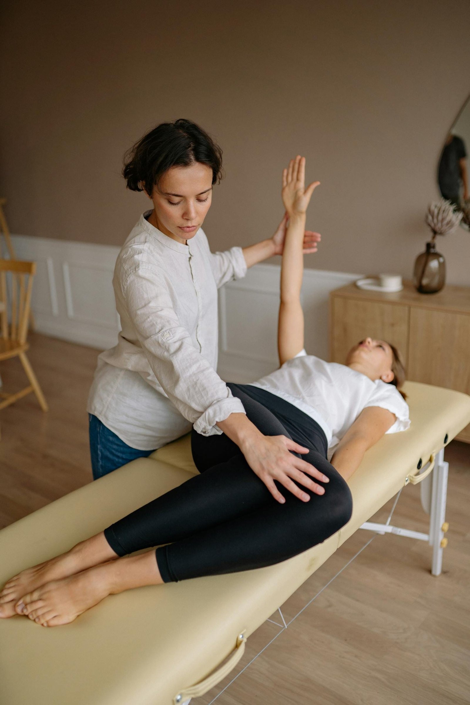 Physiotherapist aids woman with therapeutic exercises indoors.