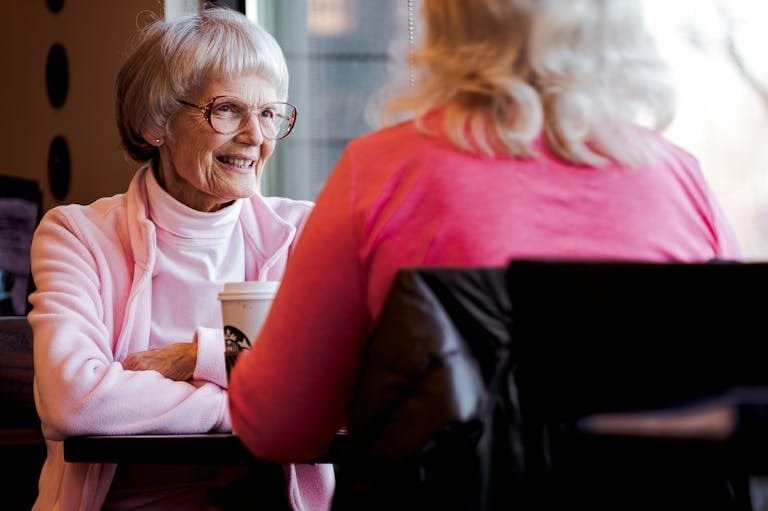 Senior women sharing a joyful conversation over coffee in a cozy indoor setting.